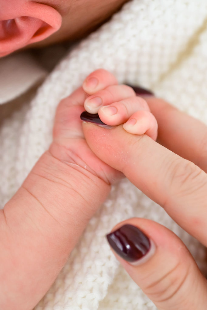 closeup photo of newborn photoshoot showing baby holding hands with mum