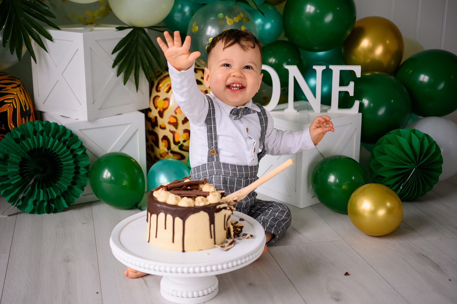 Little boy eating cake surrounded by green balloons