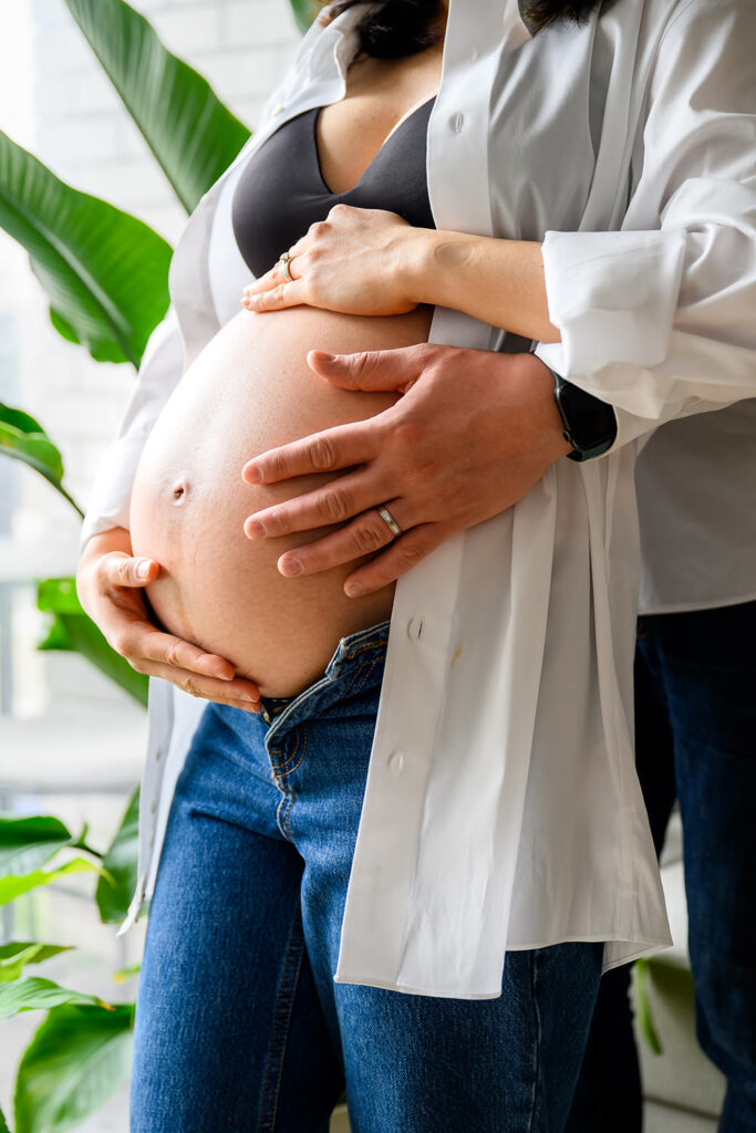 Pregnant woman and partner holding her baby bump during a relaxed maternity photoshoot at home in Nottingham